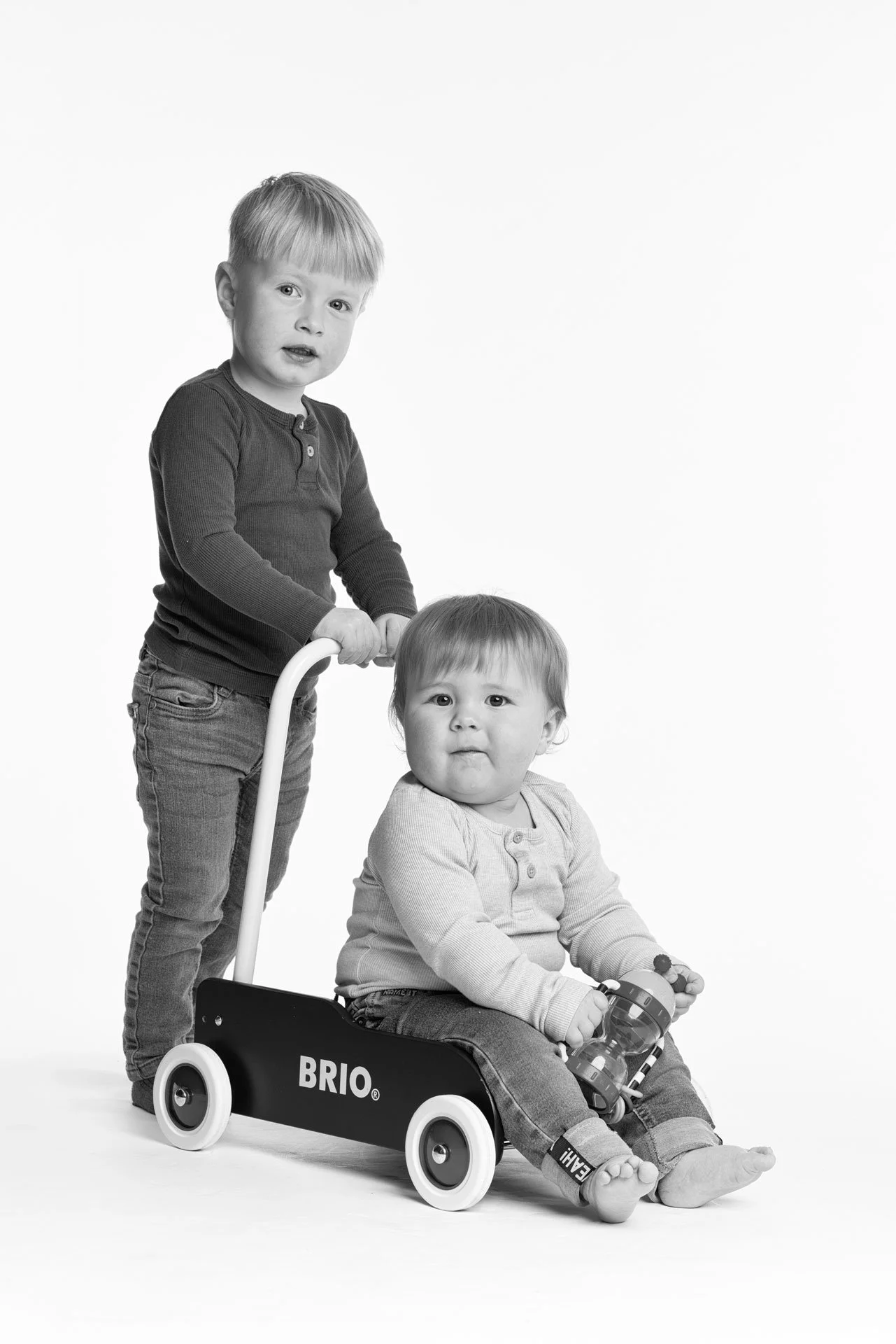 To børn, en ældre dreng og en yngre dreng, i et sort-hvidt foto. Den ældre dreng står bag en legetøjsvogn med den yngre dreng siddende i den.