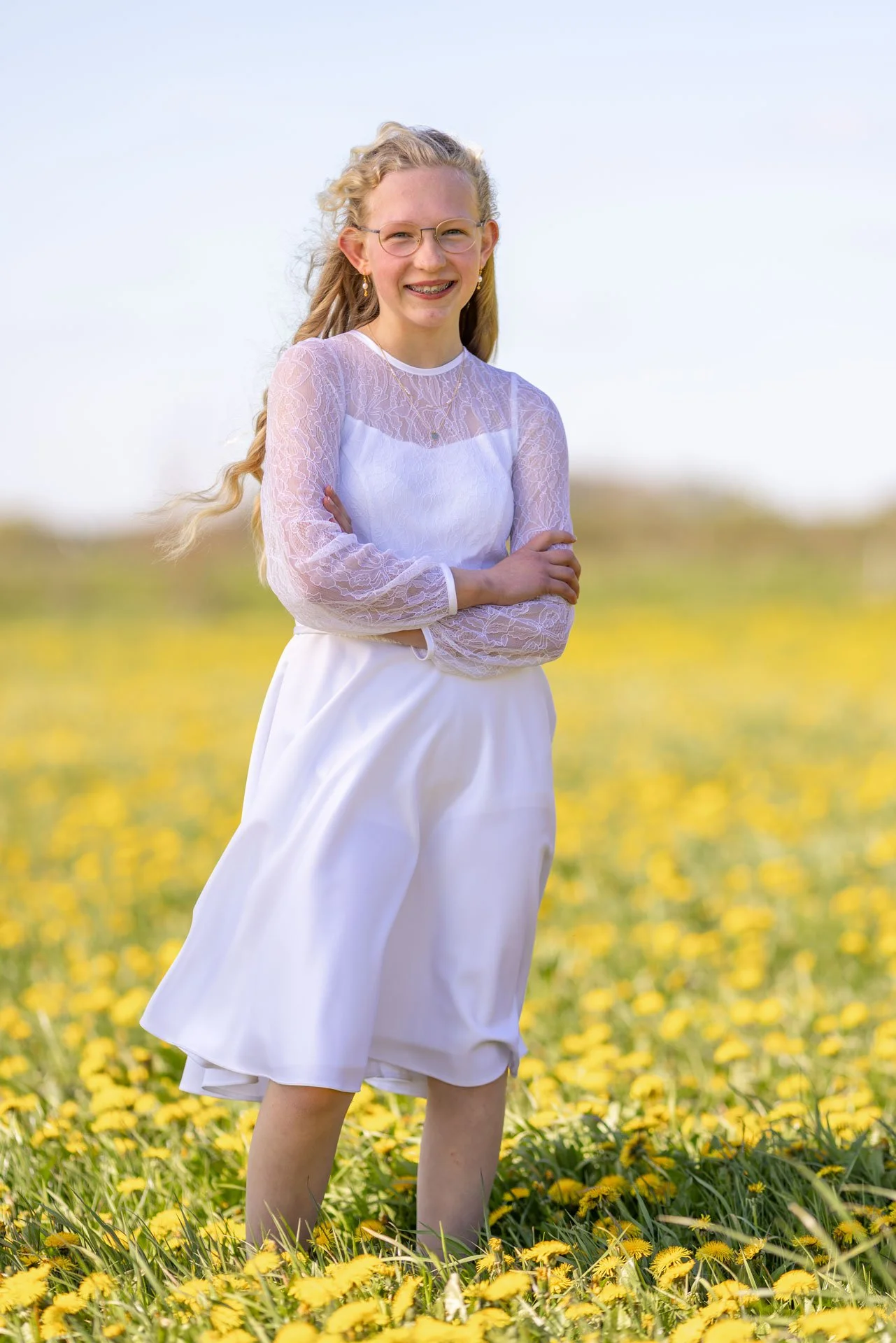 En kvinde står i en mark med gule blomster iført en hvid kjole og ser glad ud.