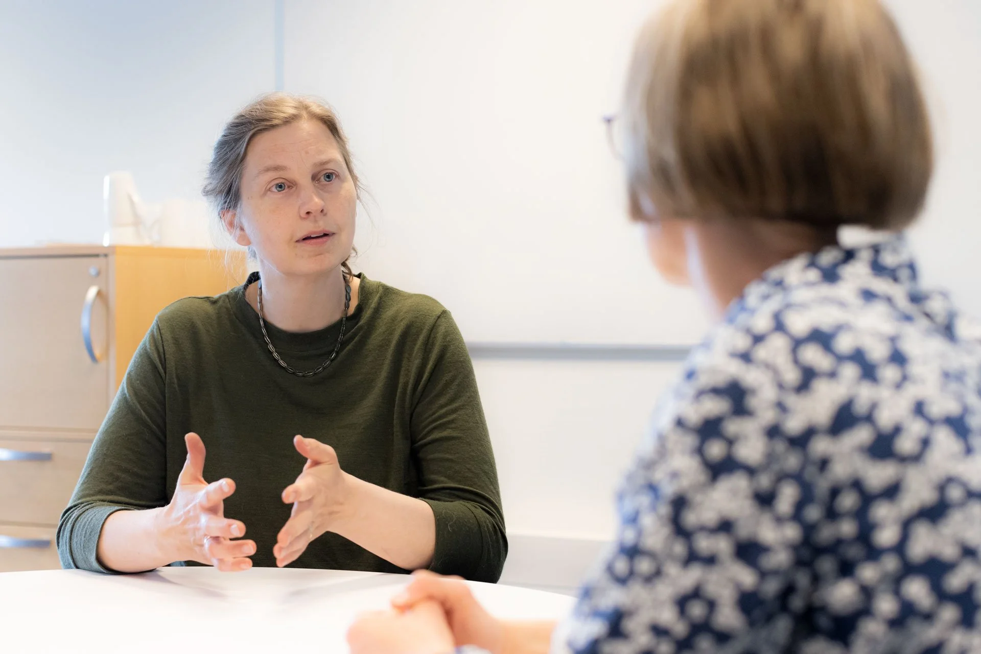 To kvinder i samtale, der sidder ved et bord i et mødelokale.