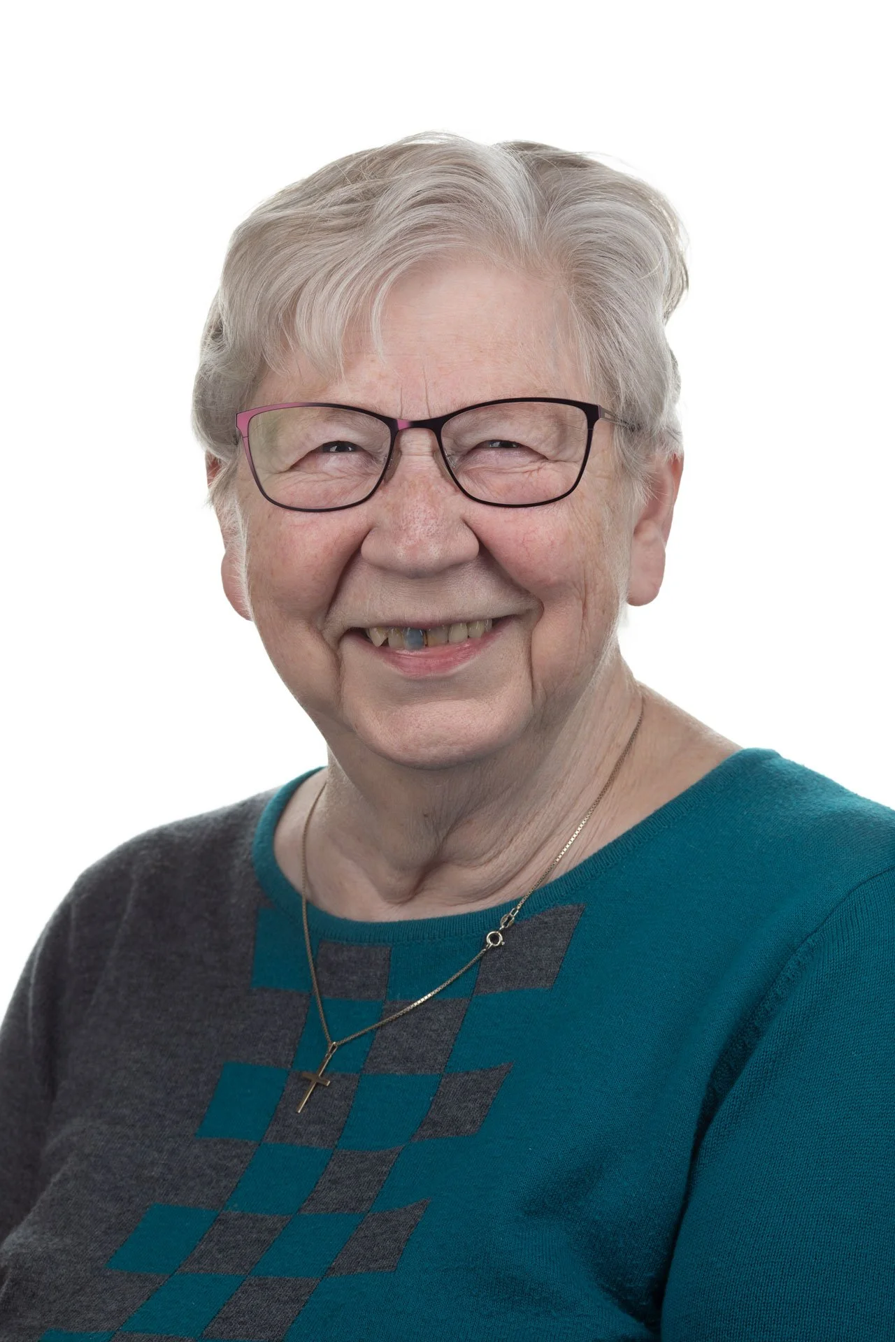 Et portrætfoto af en ældre kvinde med gråt hår, briller og smilende ansigt mod en hvid baggrund.