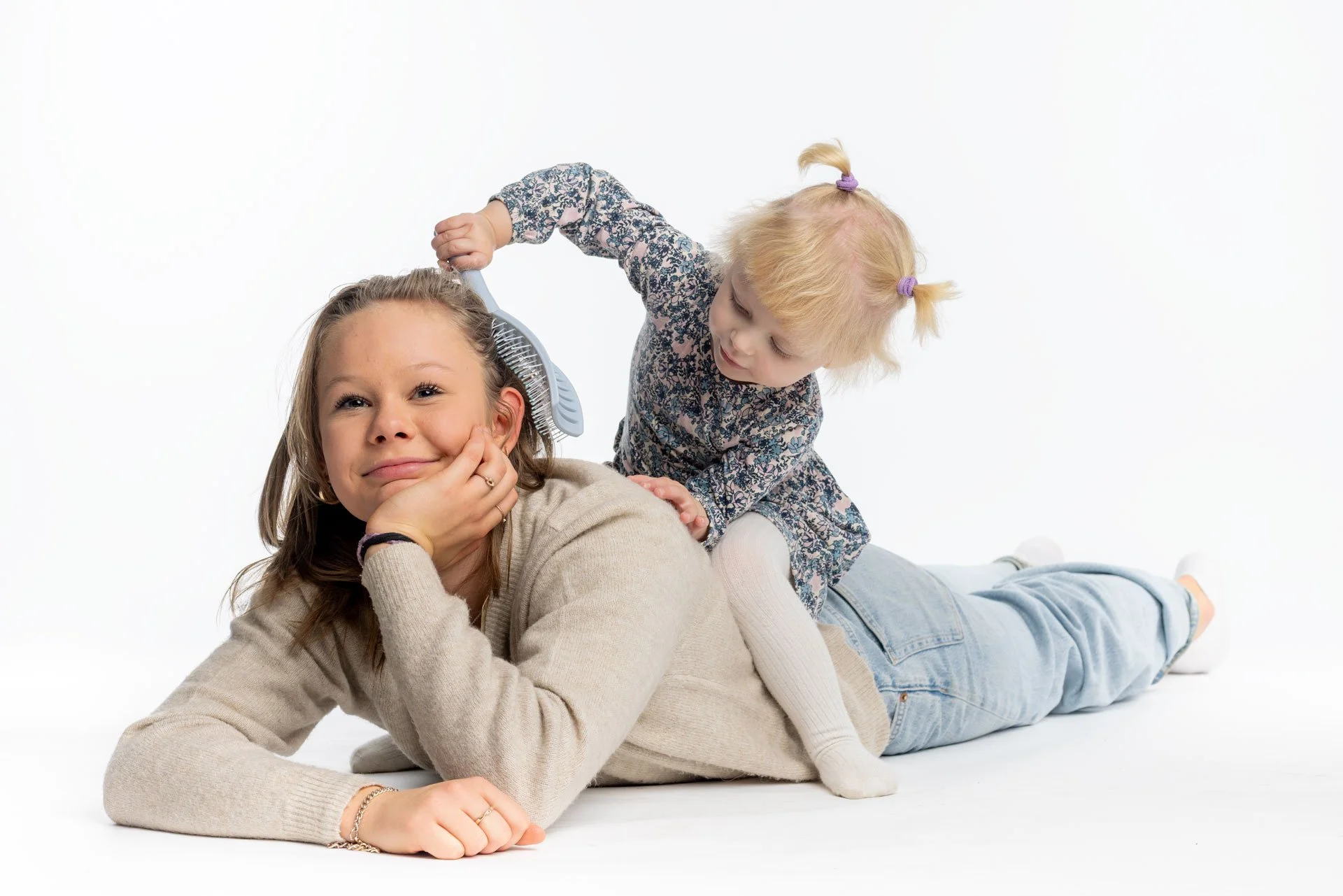 To unge piger leger på gulvet, den ene ligger ned og smiler, mens den anden børster hendes hår.