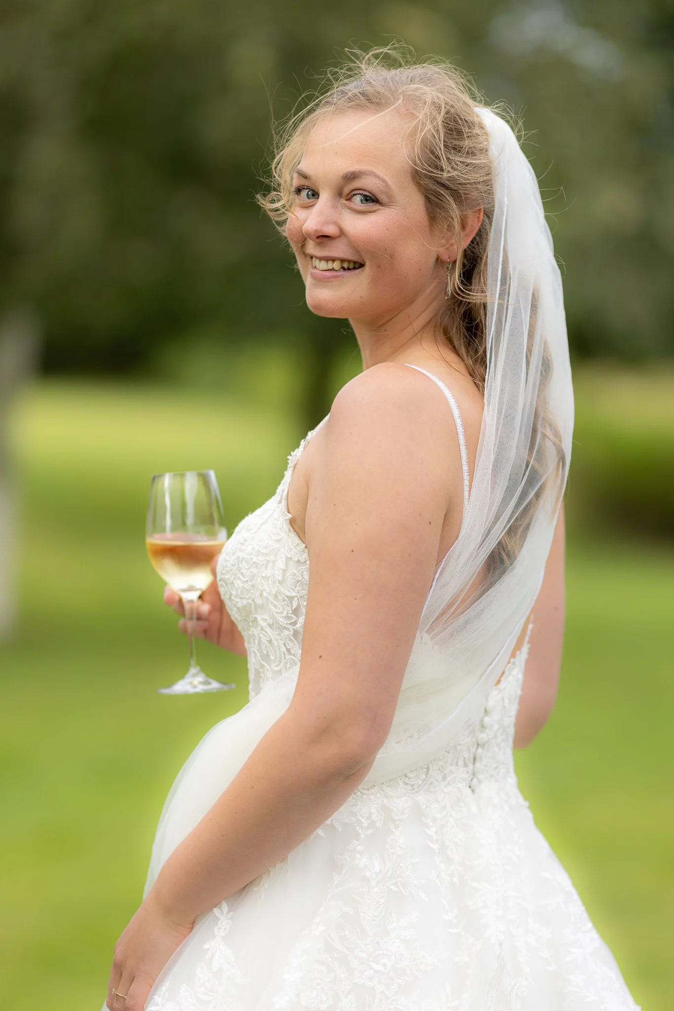 En glad kvinde i en hvid brudekjole holder et glas vin og smiler.