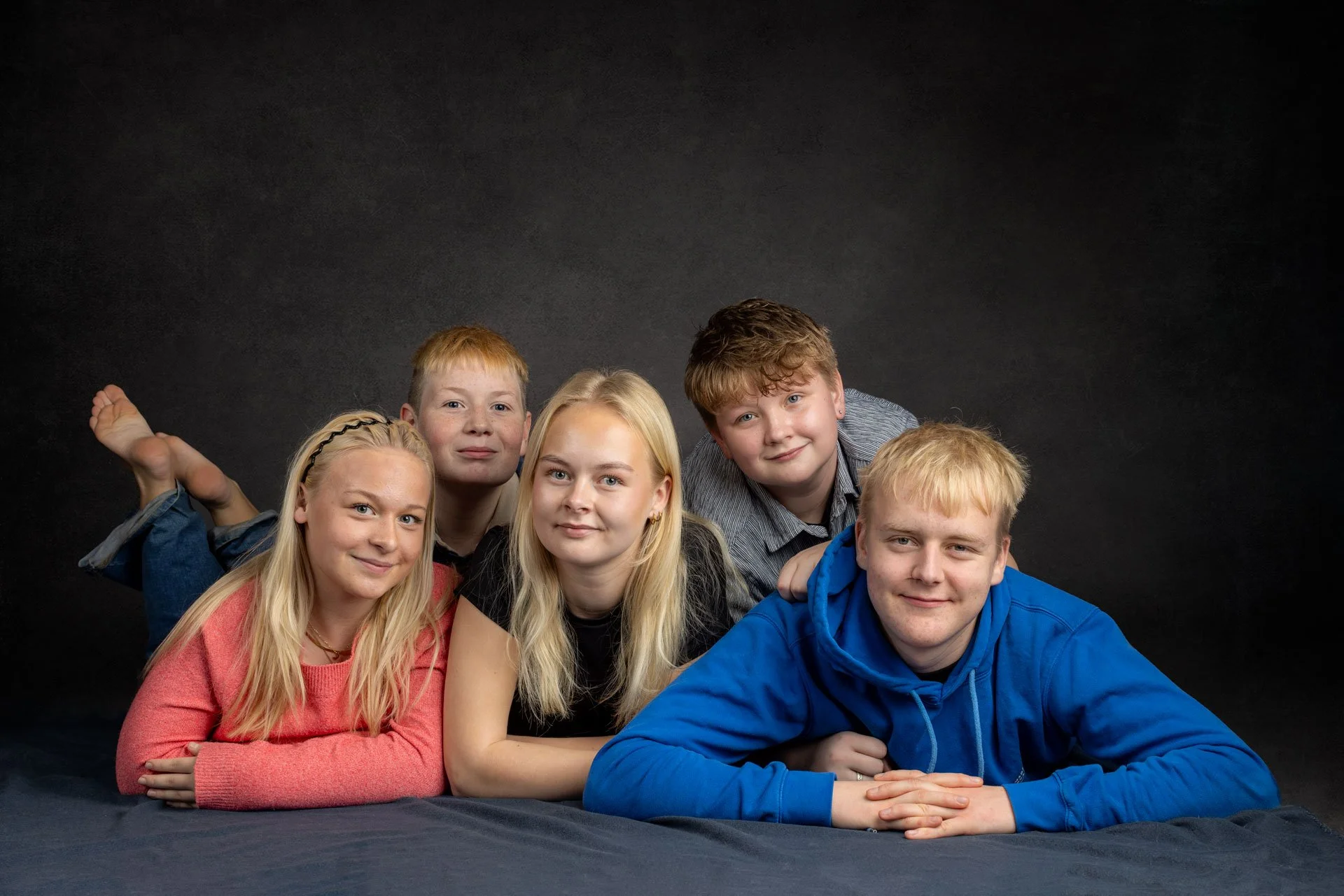 Syv unge mennesker, fem drenge og to piger, ligger på en sort baggrund, og ser smilede mod kameraet.