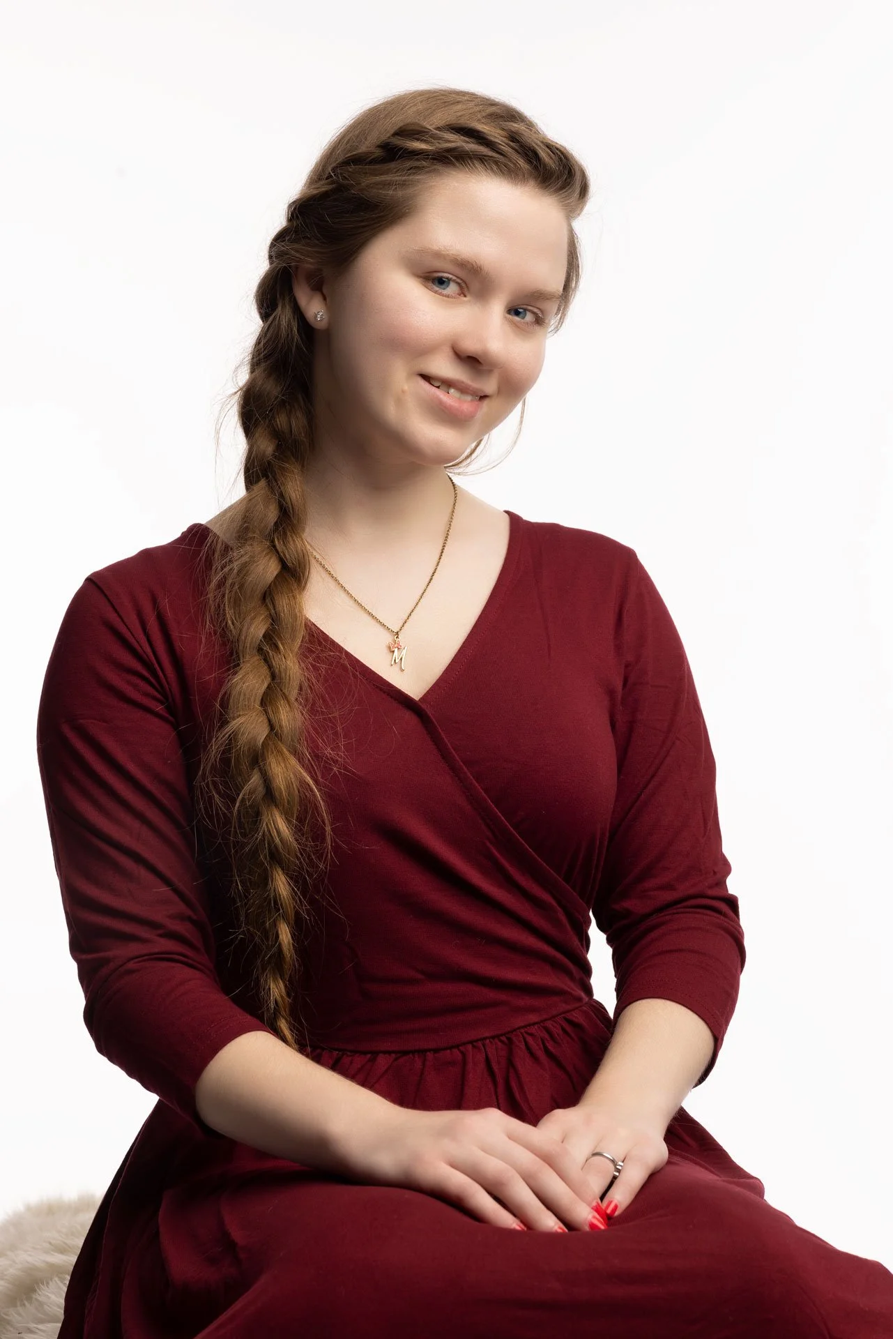 Kvinde med lang, mellemlangt hår i flet, iført en rød kjole, sidder mod en hvid baggrund, smilende.