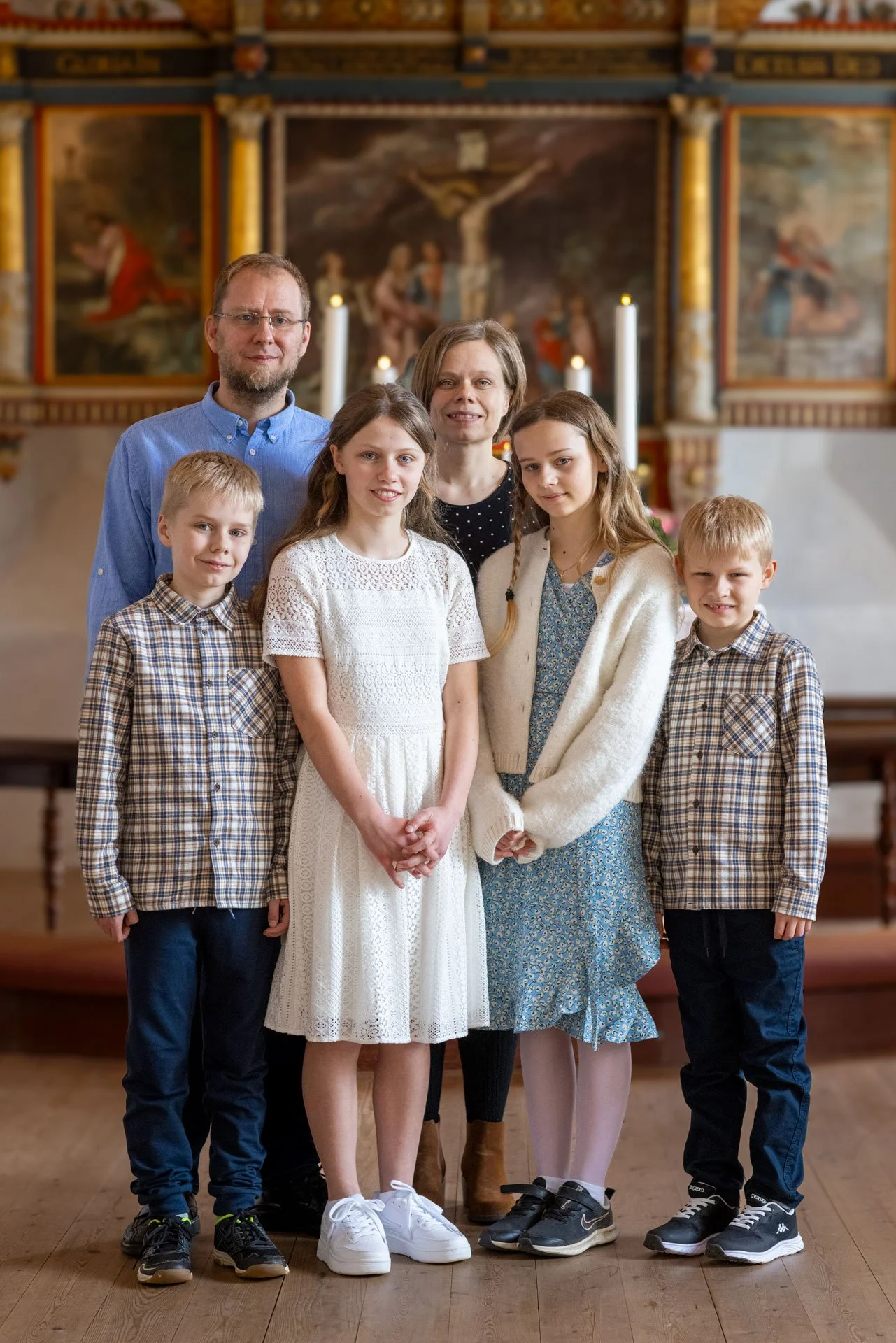 En gruppe mennesker står inde i en kirke foran en altertavle med lysende stearinlys.