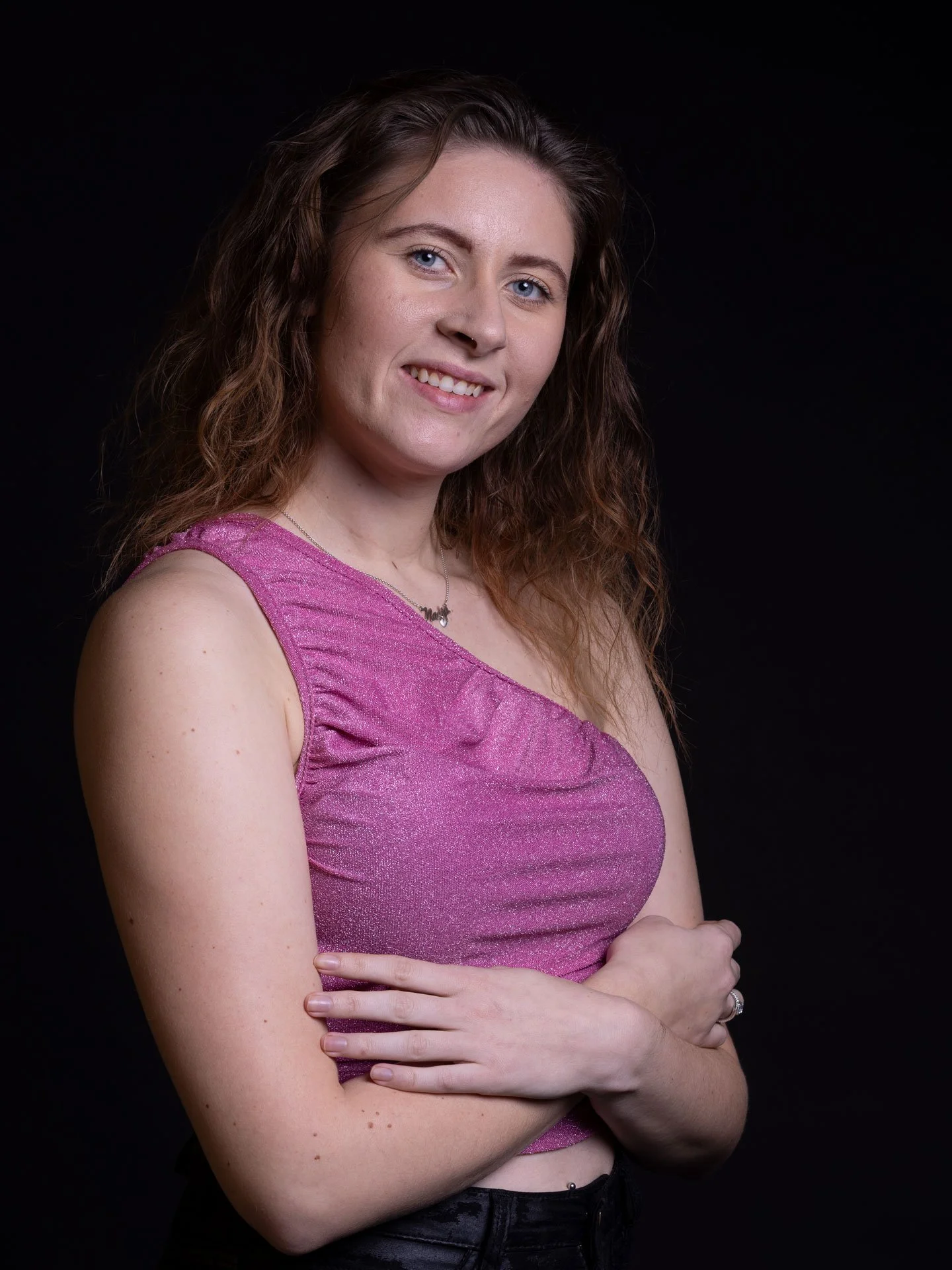 Portræt af en kvinde med brunt, krøllet hår, iført en pink top, smilende, mod en sort baggrund.