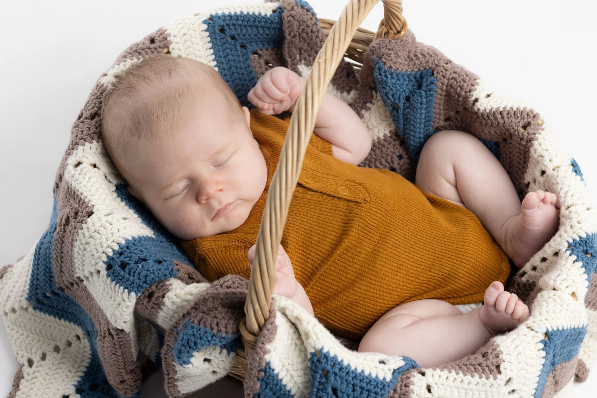 Søvnende baby i en kurv med en farvet, strikket dyne og en brun body.