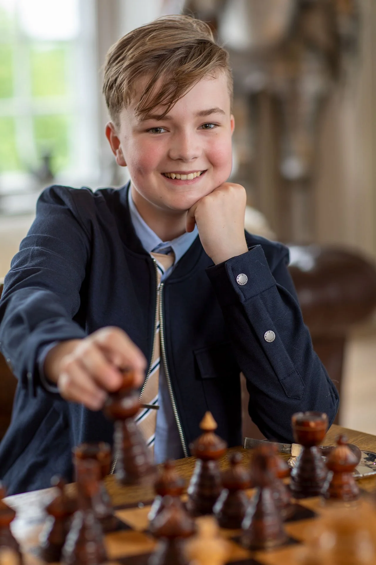 Ung mand smiler, sidder ved et skakbræt, klar til at flytte en brik.