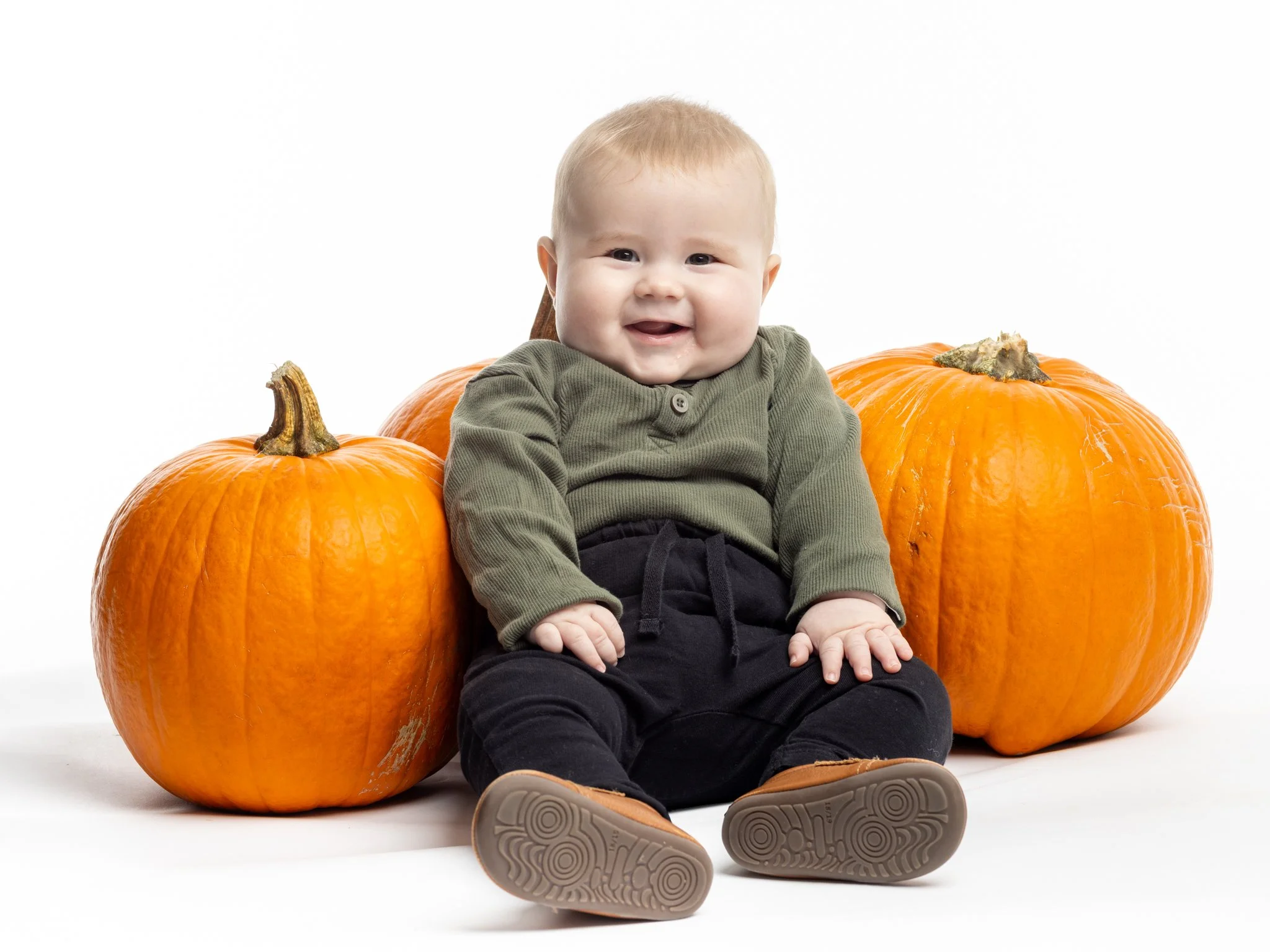 En smilende baby sidder mellem tre græskar på en hvid baggrund.