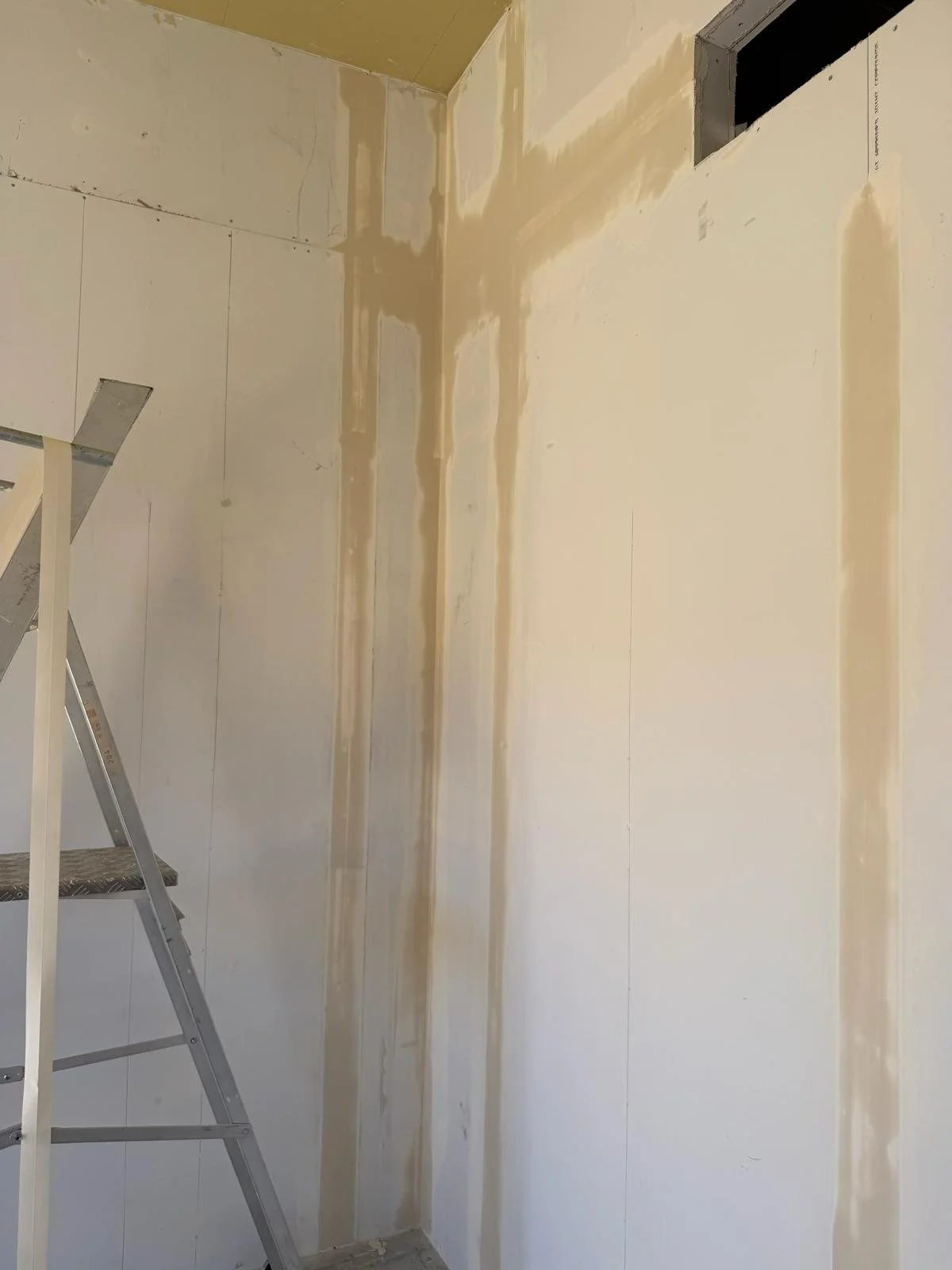 Interior wall with water damage and staining, an aluminum ladder on the left side, and an open vent in the upper right corner.