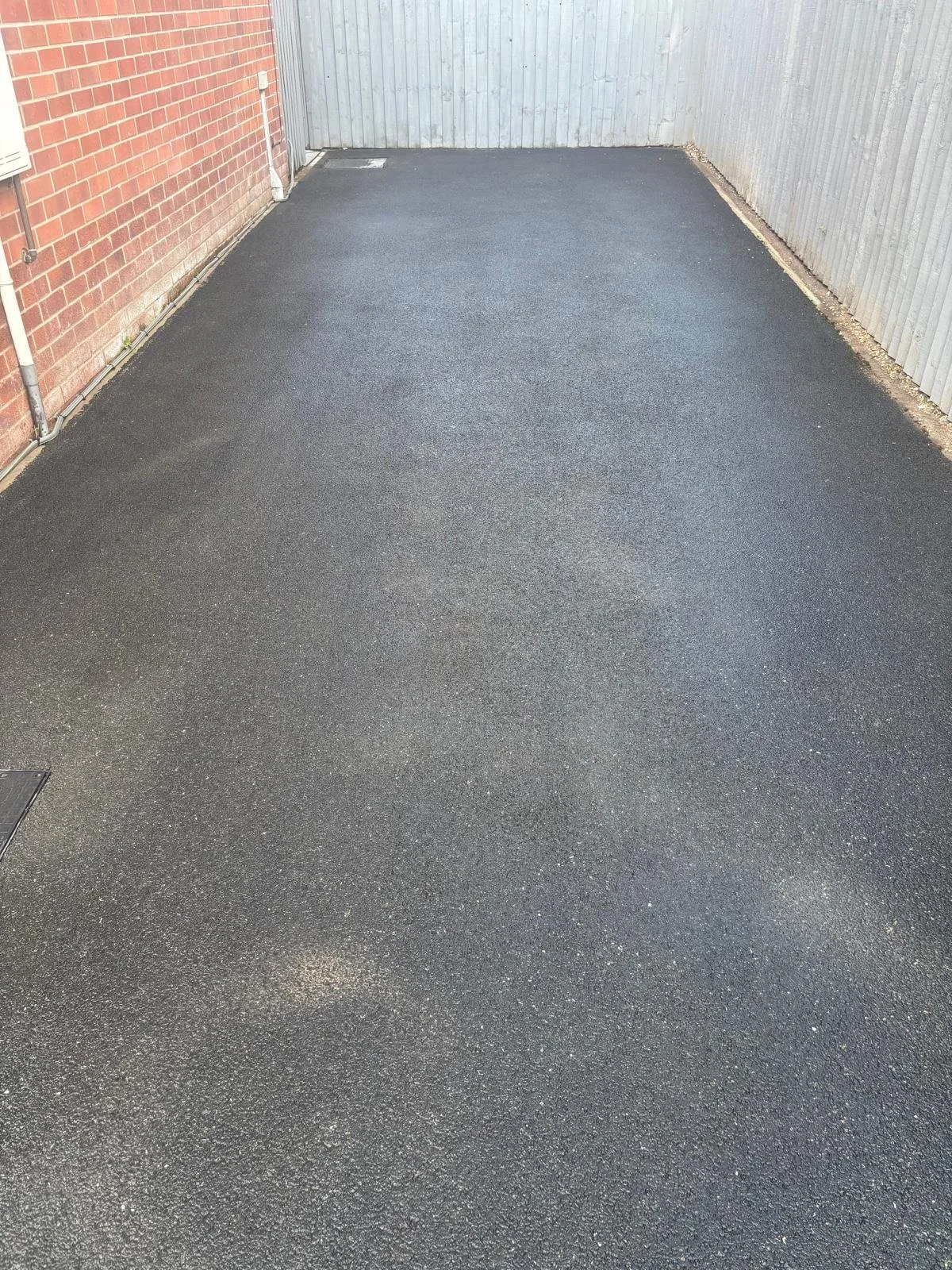 Freshly paved asphalt in a small enclosed yard with brick and wooden fences.