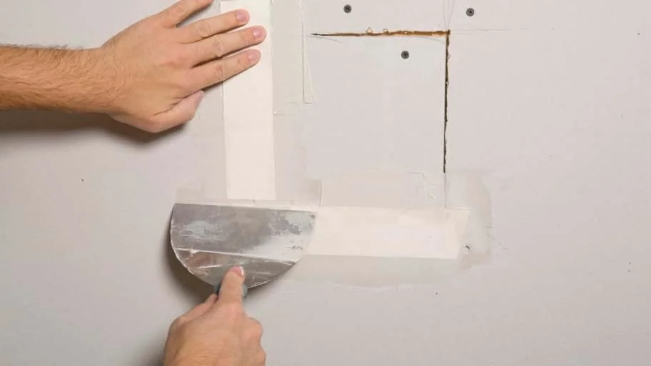 Person removing a drywall patch to reveal a hole in the wall.