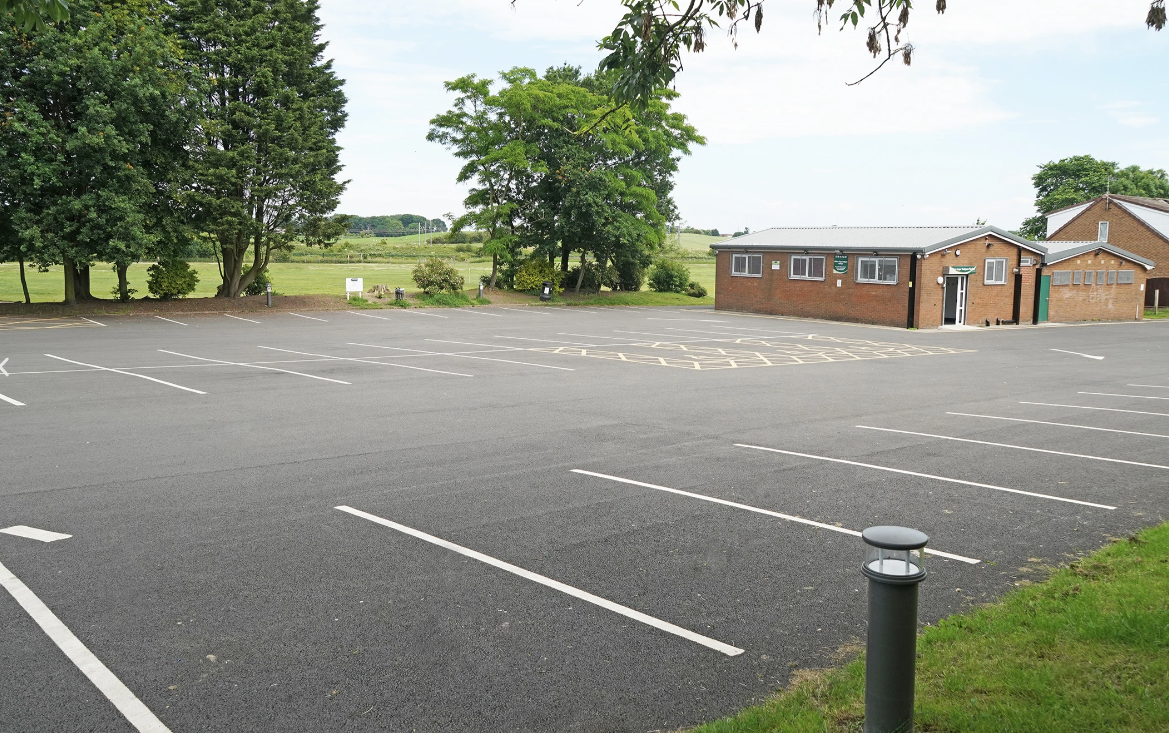 Empty parking lot with a small brick building and trees in the background.