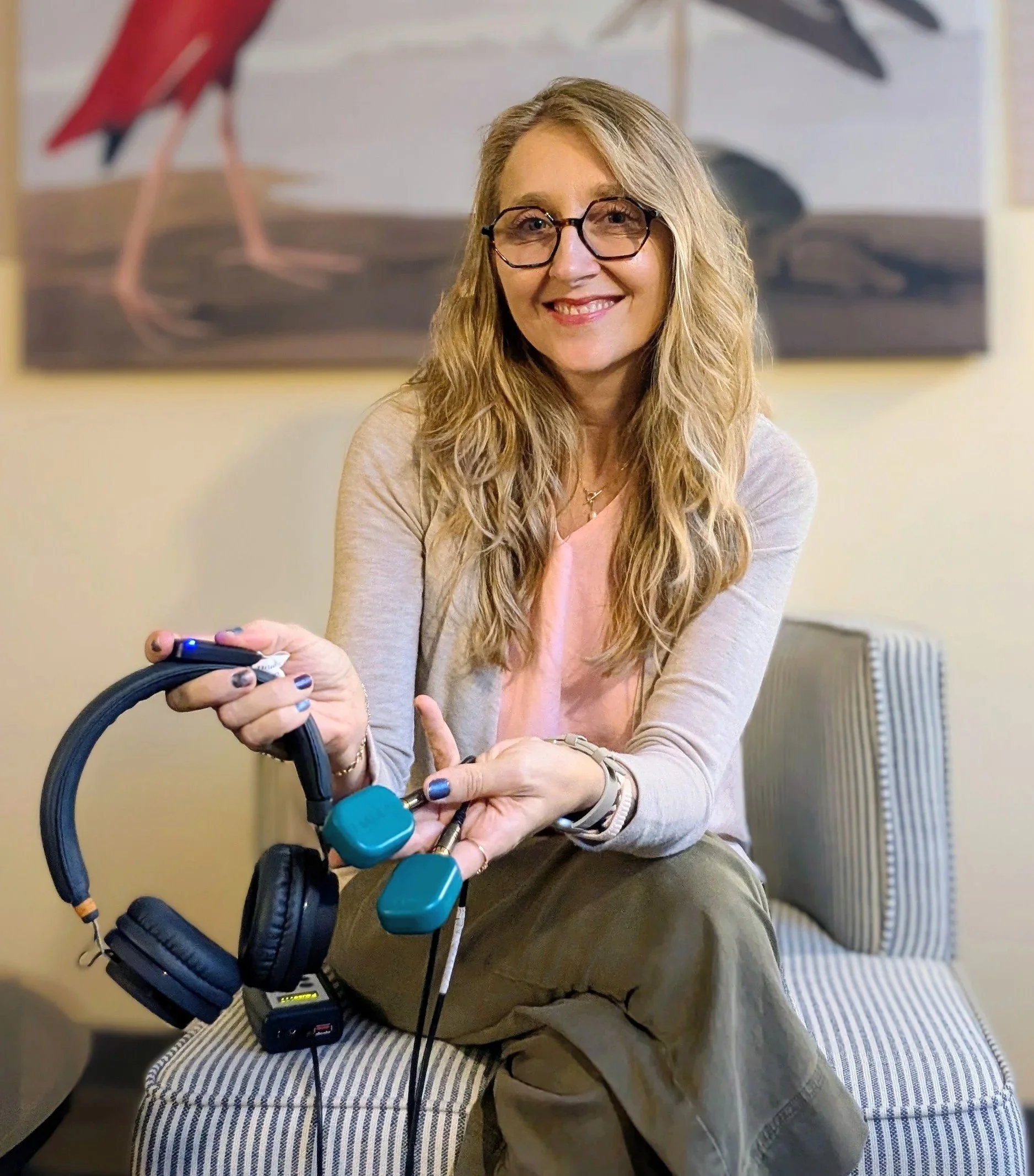 Smiling woman wearing glasses demonstrates exercise equipment with headphones and small teal weights