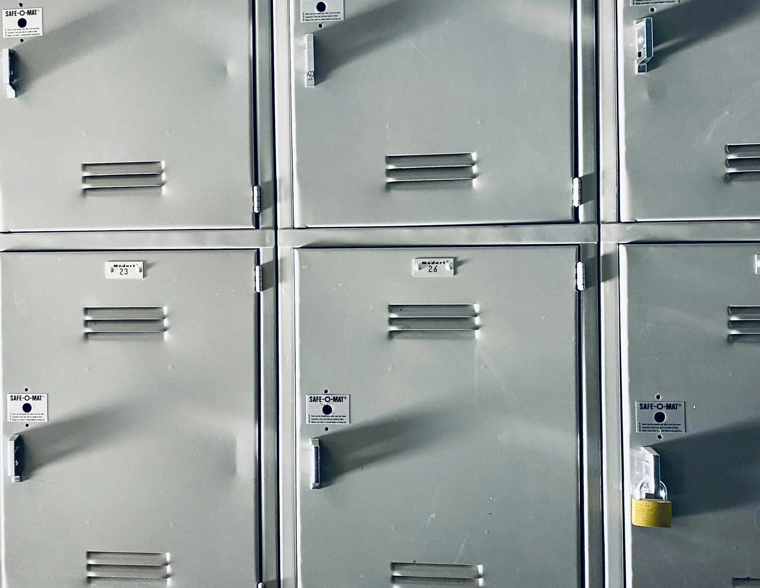A row of grey, industrial steel lockers, one with a padlock. This illustrates the concept that basic operational tools are more important than wellness perks.