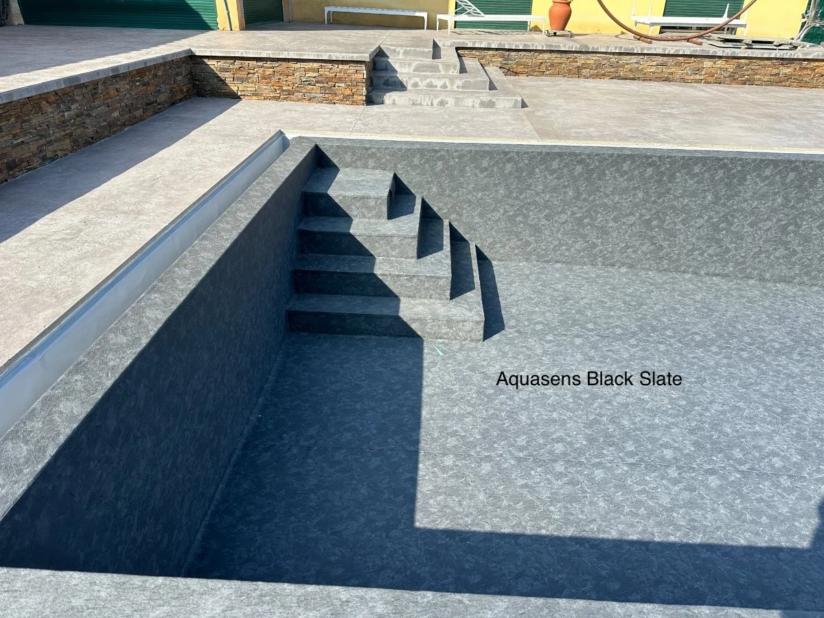 Une piscine creusée avec un revêtement en Slate noir Aquasens, entourée d'une terrasse en pierre, avec des escaliers intégrés.