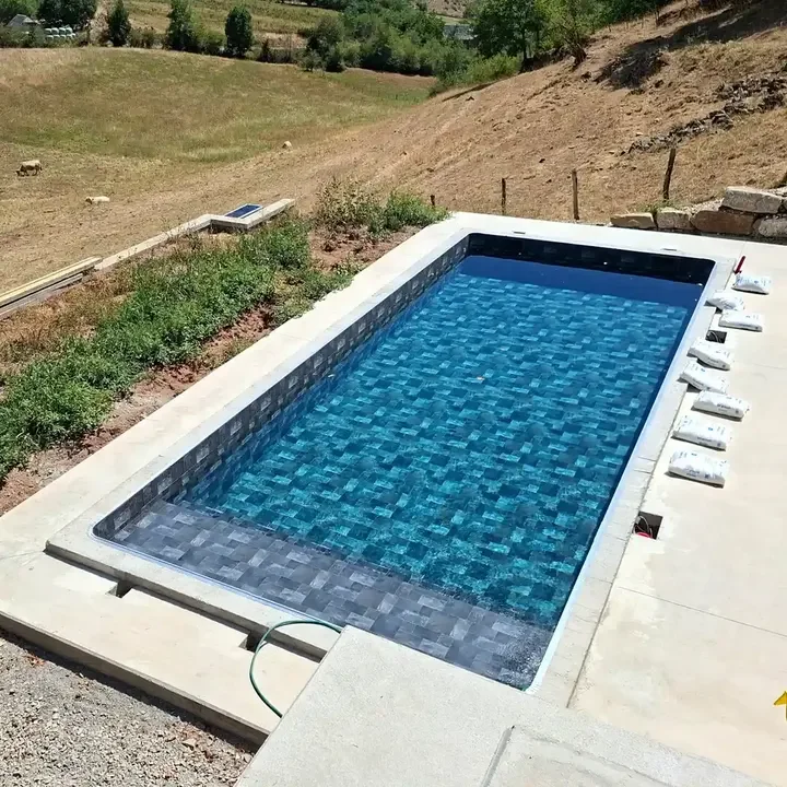 Petite piscine rectangulaire avec des carreaux bleus, située dans un paysage rural avec des collines et des herbes sèches.