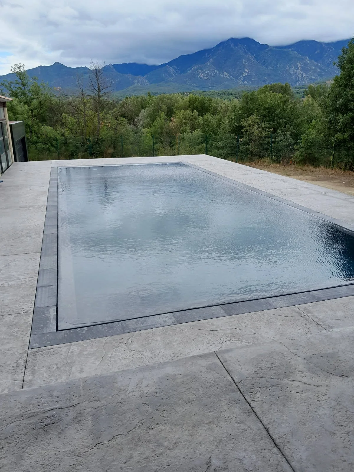 Piscine à débordement en extérieur avec vue sur des montagnes et un ciel nuageux.
