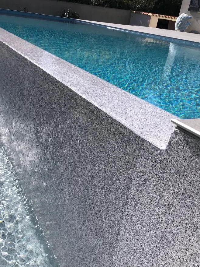 Gros plan sur une membrane  armee piscine posée sur un débordement d'un bleu limpide, l'eau dévalant un rebord en pierre pour se déverser dans un bassin peu profond en contrebas.