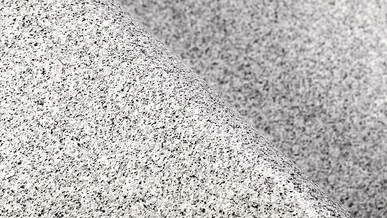 Gros plan sur un granit texturé et moucheté avec un pli diagonal, ressemblant à l'aspect des surfaces de piscines armées de membranes PVC.