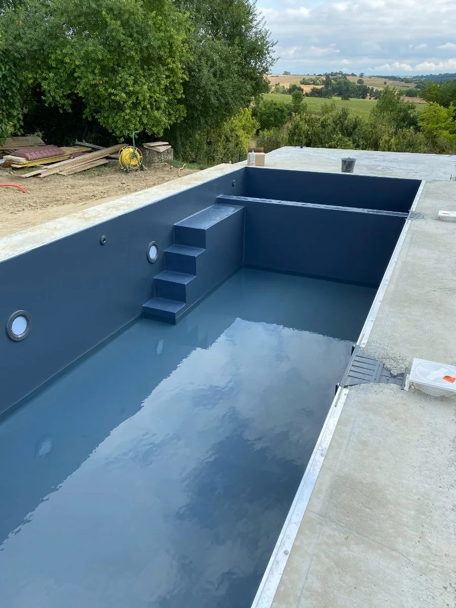 Piscine en construction avec une surface bleue et une vue sur la campagne environnante.