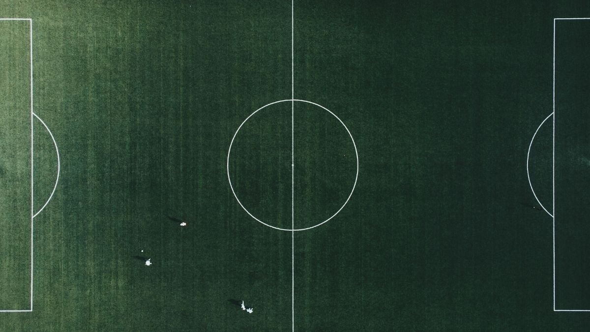 An aerial view of an empty soccer field with visible grass and white boundary lines.