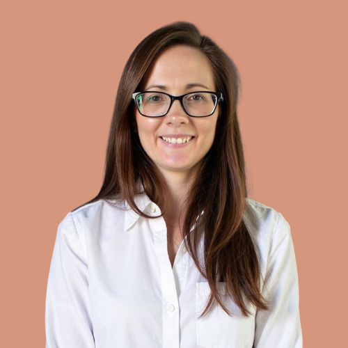 A woman with long brown hair, glasses, and a white shirt smiling against a brown background.