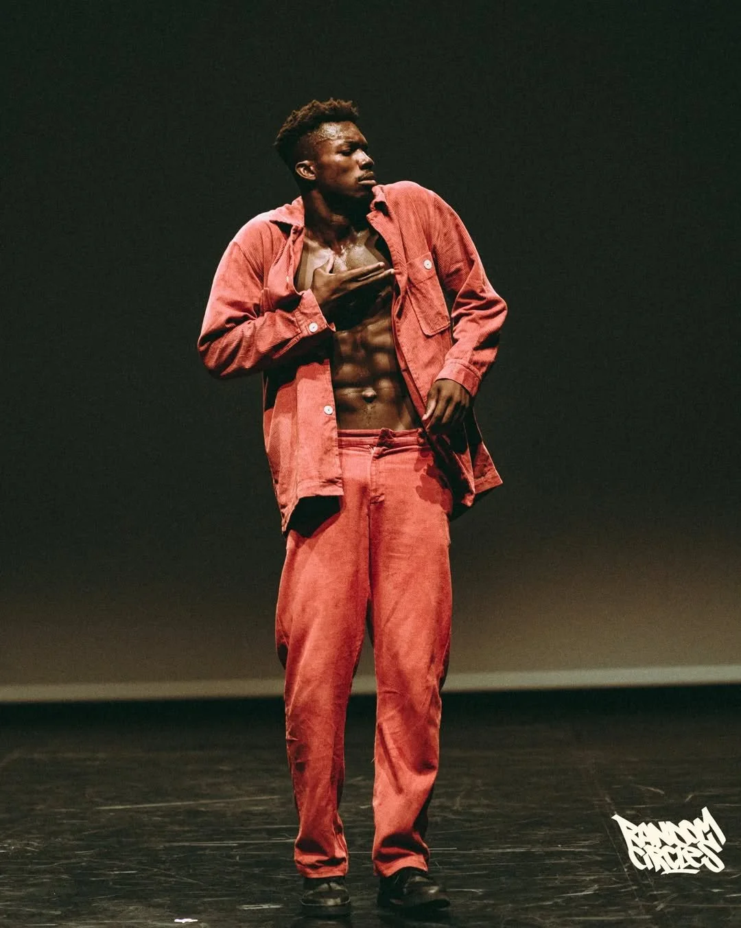 A shirtless man in red pants and a red jacket performing on stage.