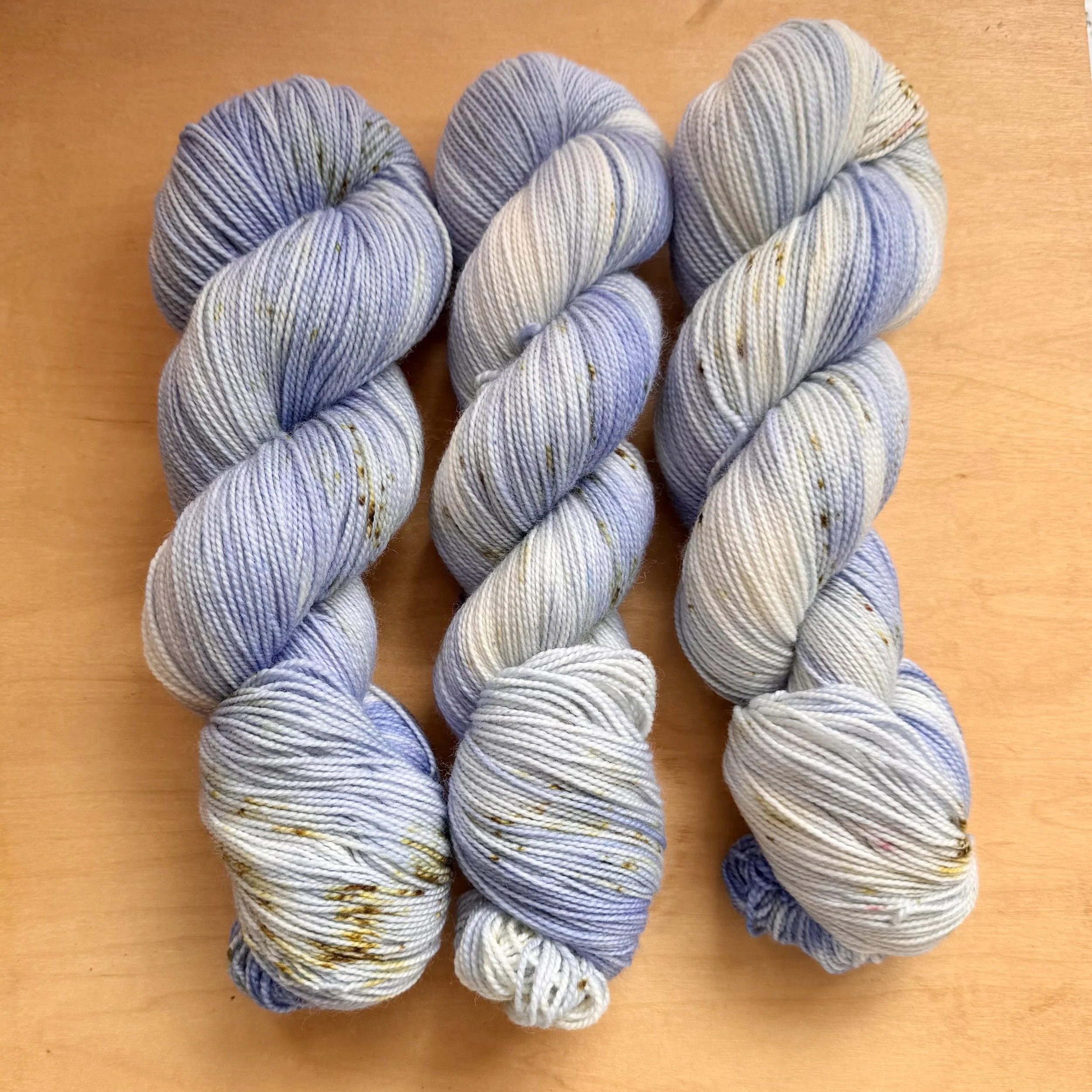 Three skeins of light blue, speckled yarn twisted into hanks on a wooden surface.