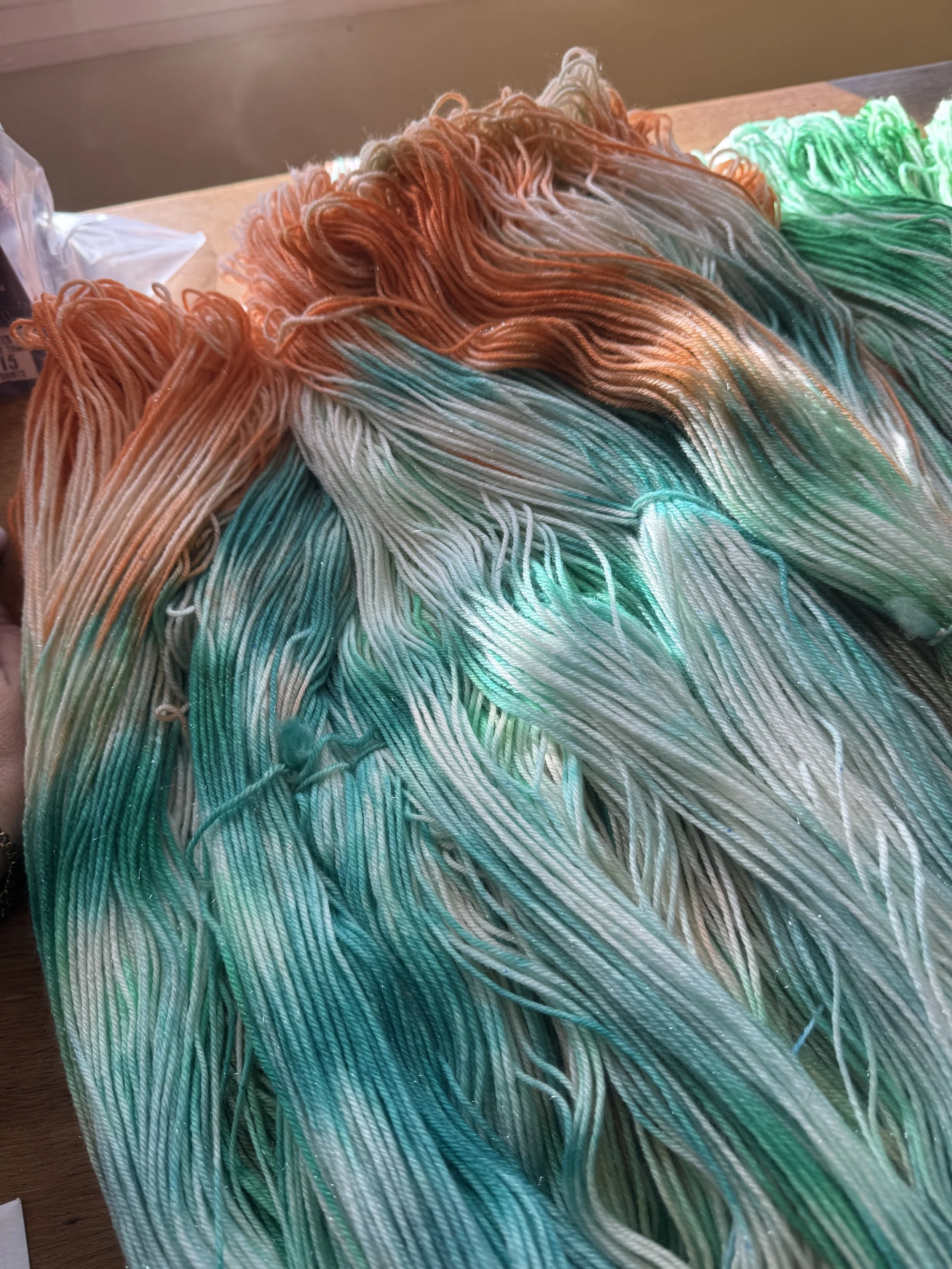 Colorful hand dyed yarns in shades of orange, green, and cream laid out on a wooden surface. Showgirl inspired.