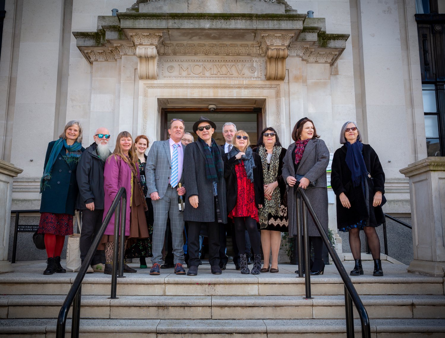 A group of people standing on the steps outside a historic building with ornate stone details.