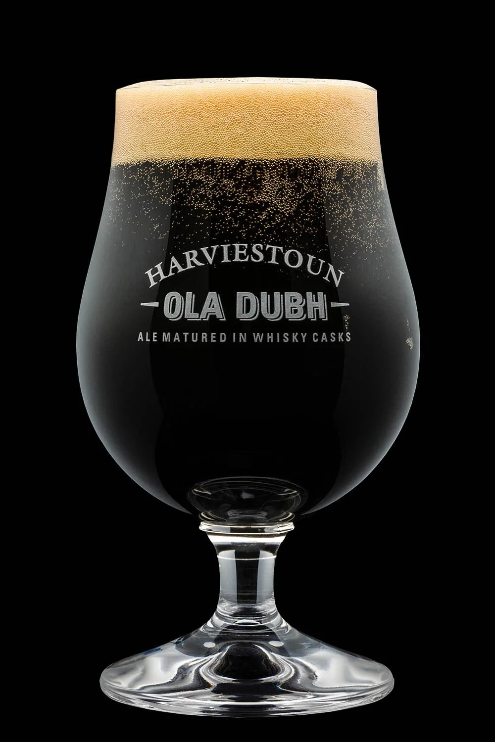 A glass of dark stout beer with a thick foam head, branded with 'Harviestoun Ola Dubh Ale matured in whisky casks' against a black background.
