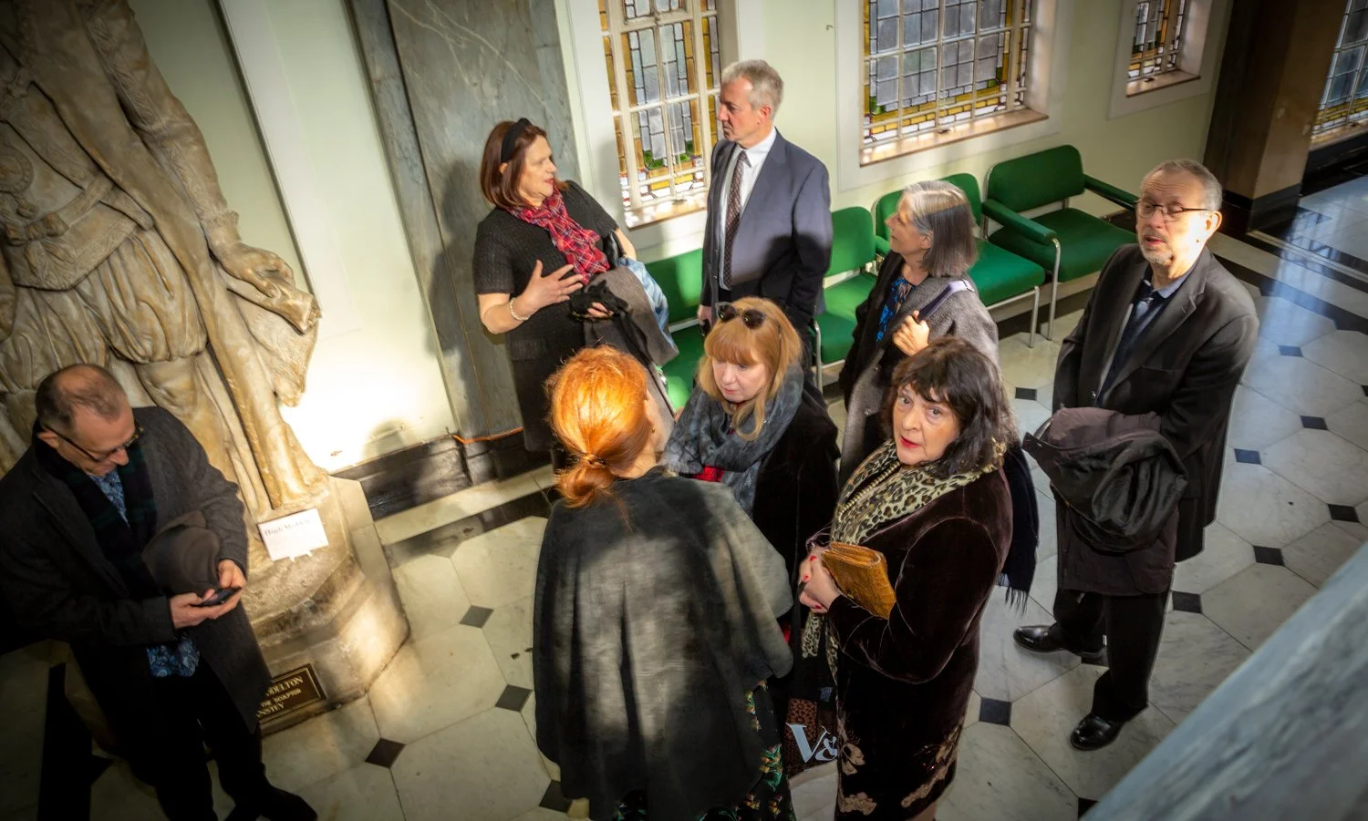 Group of people in a hallway, engaged in conversation, some standing and some sitting.