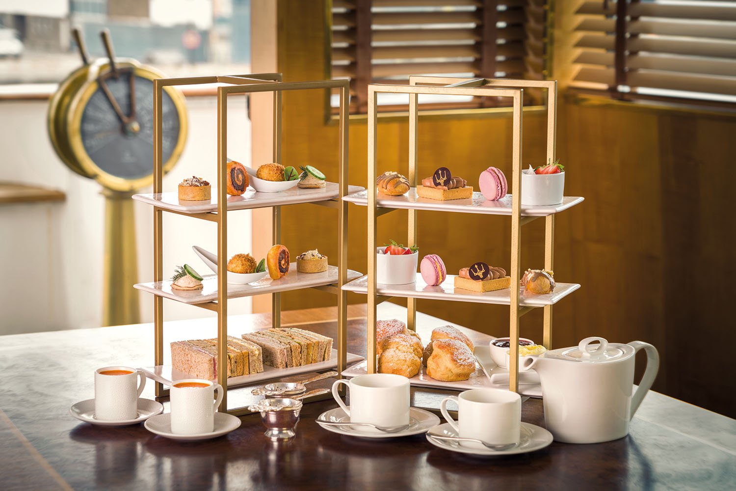 A tiered Fingal Hotel serving tray with assorted desserts and finger sandwiches on a table, with teacups and a teapot in the foreground.