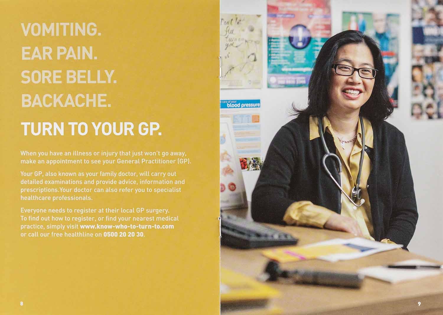 A woman sitting at a desk in a medical office closet with a smile, wearing glasses, a black sweater, and a stethoscope around her neck. The background includes posters and health-related materials.