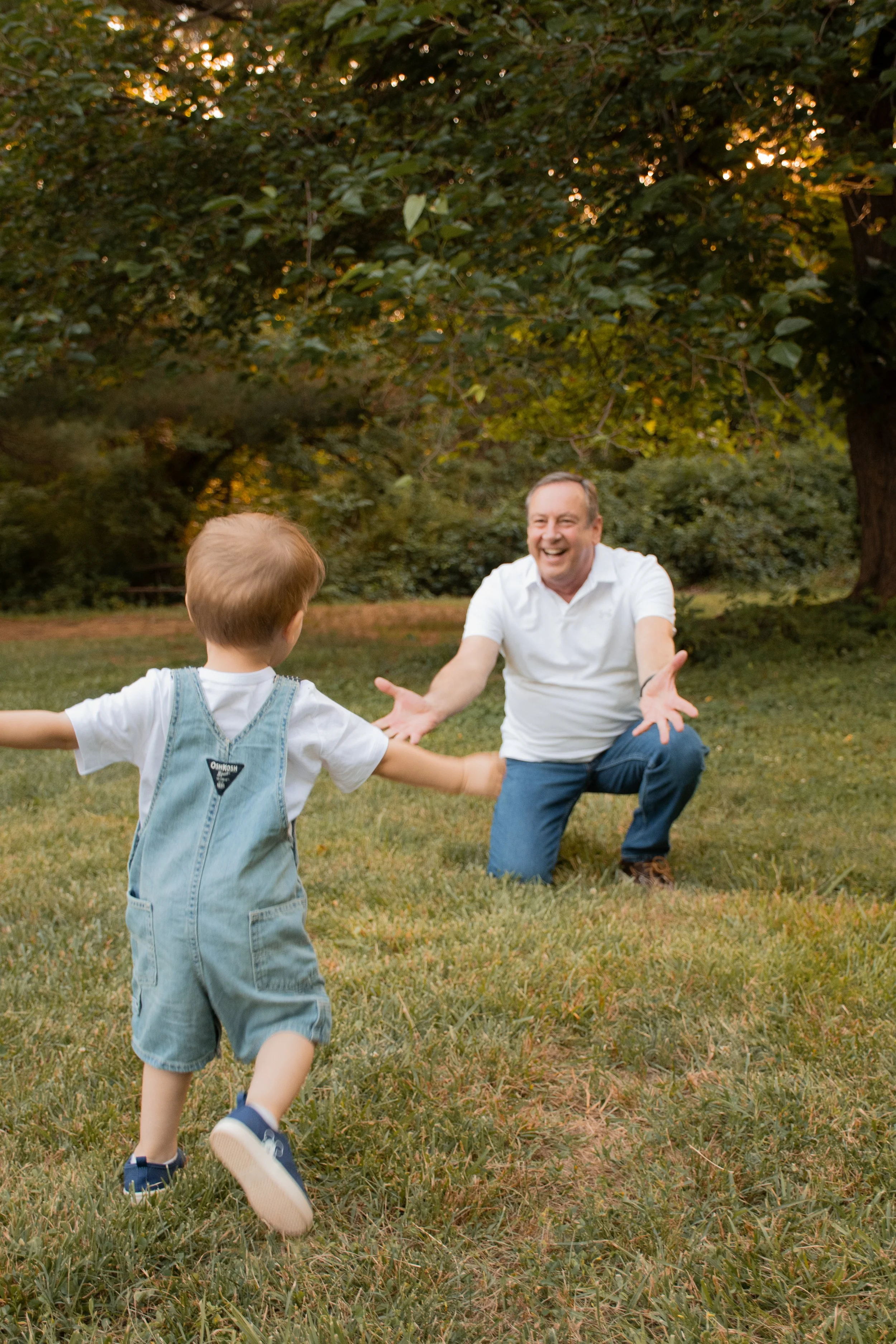  A toddler running across the grass toward a kneeling man