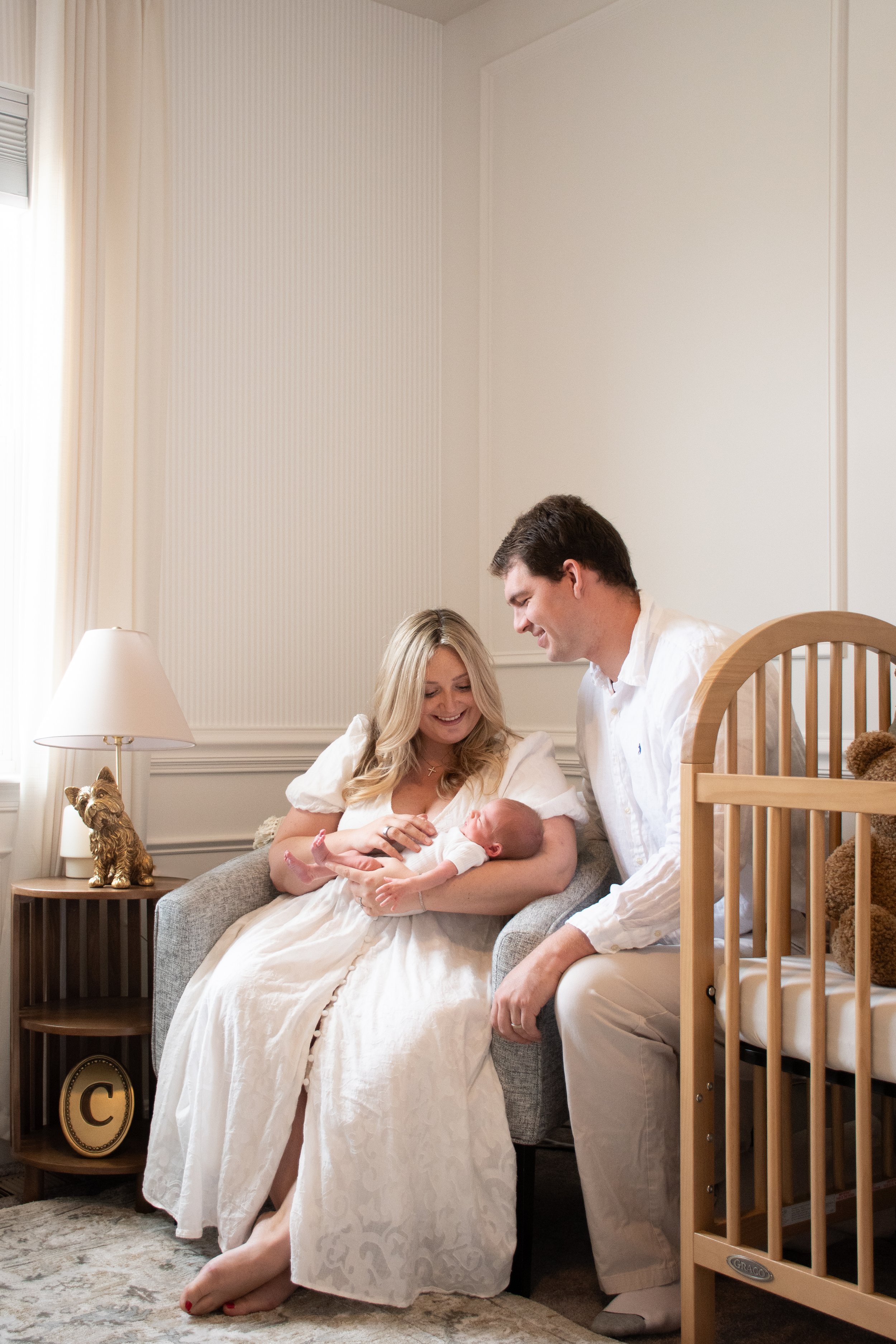  Parents seated in the nursery, the mother holding their newborn beside the crib