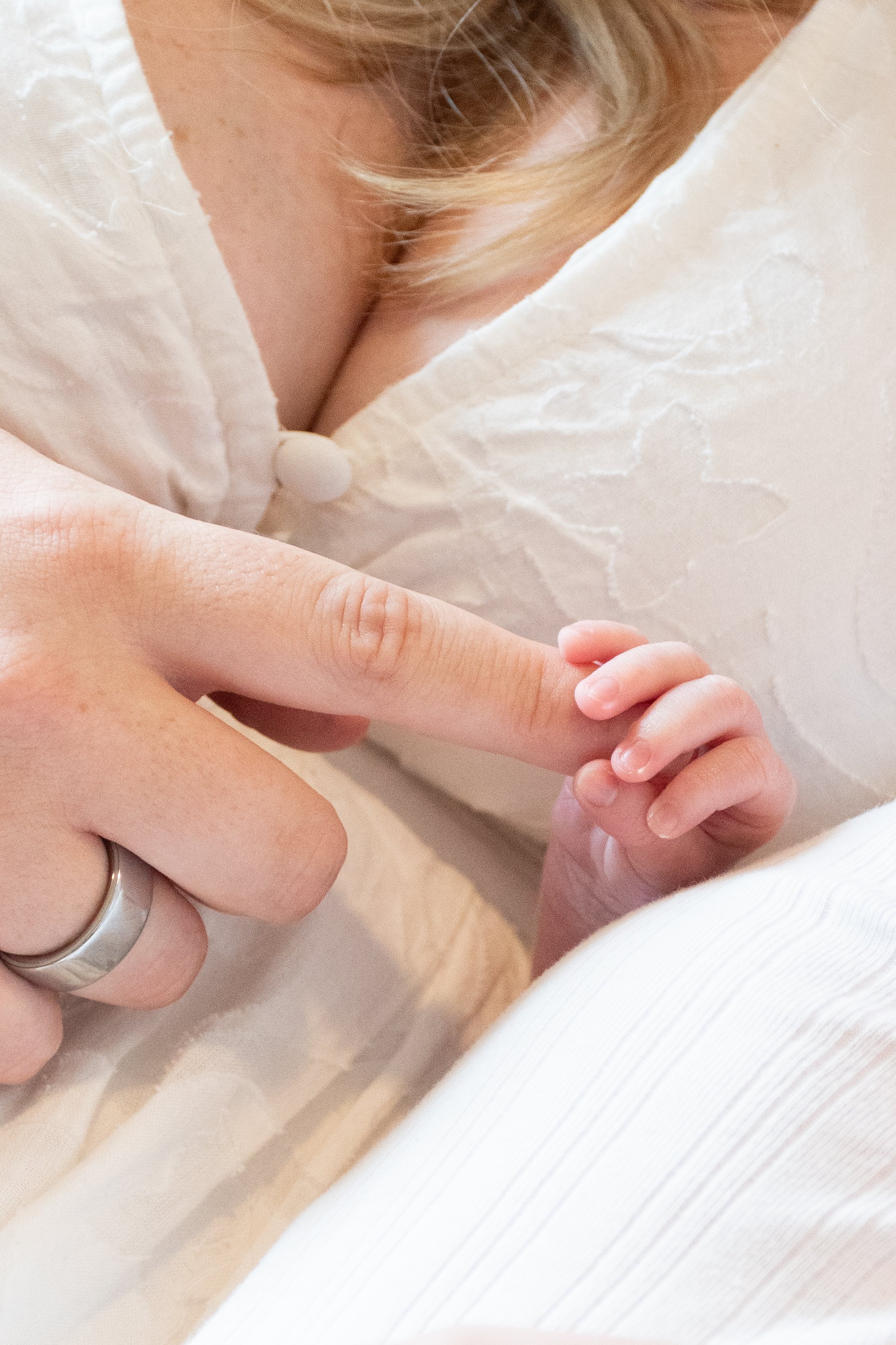 A close-up of a newborn gripping their mother's finger