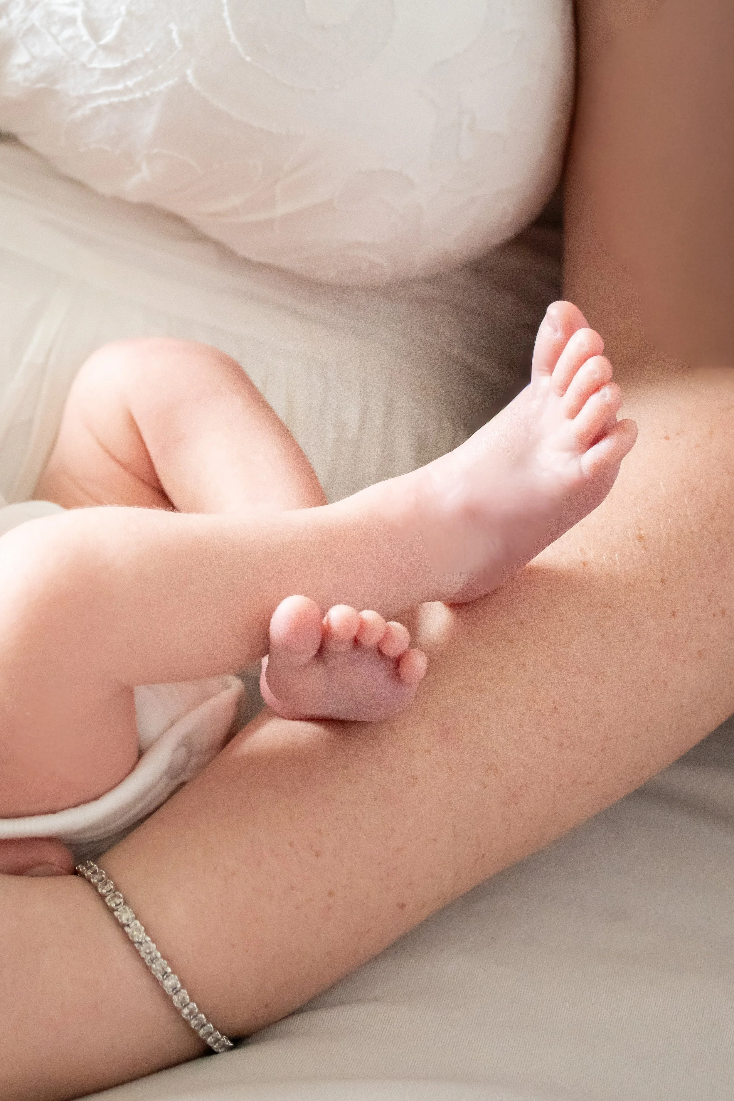 A close-up of a newborn's bare feet resting against an adult's arm
