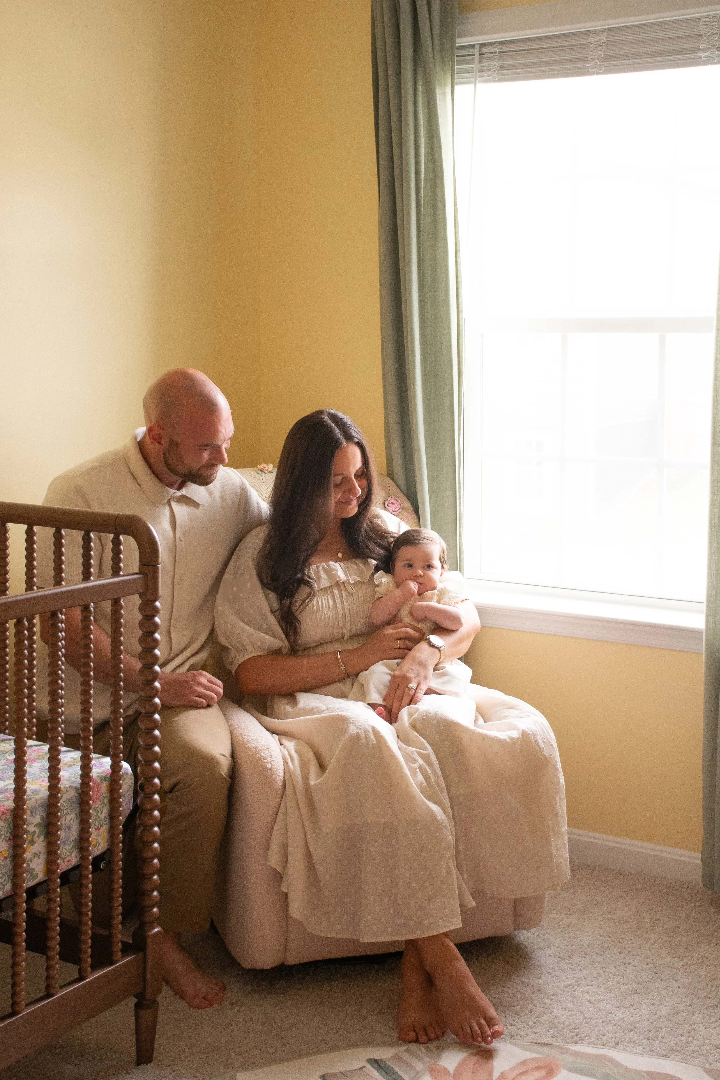 Parents sitting near a window with light streaming in, the mother holding their baby.