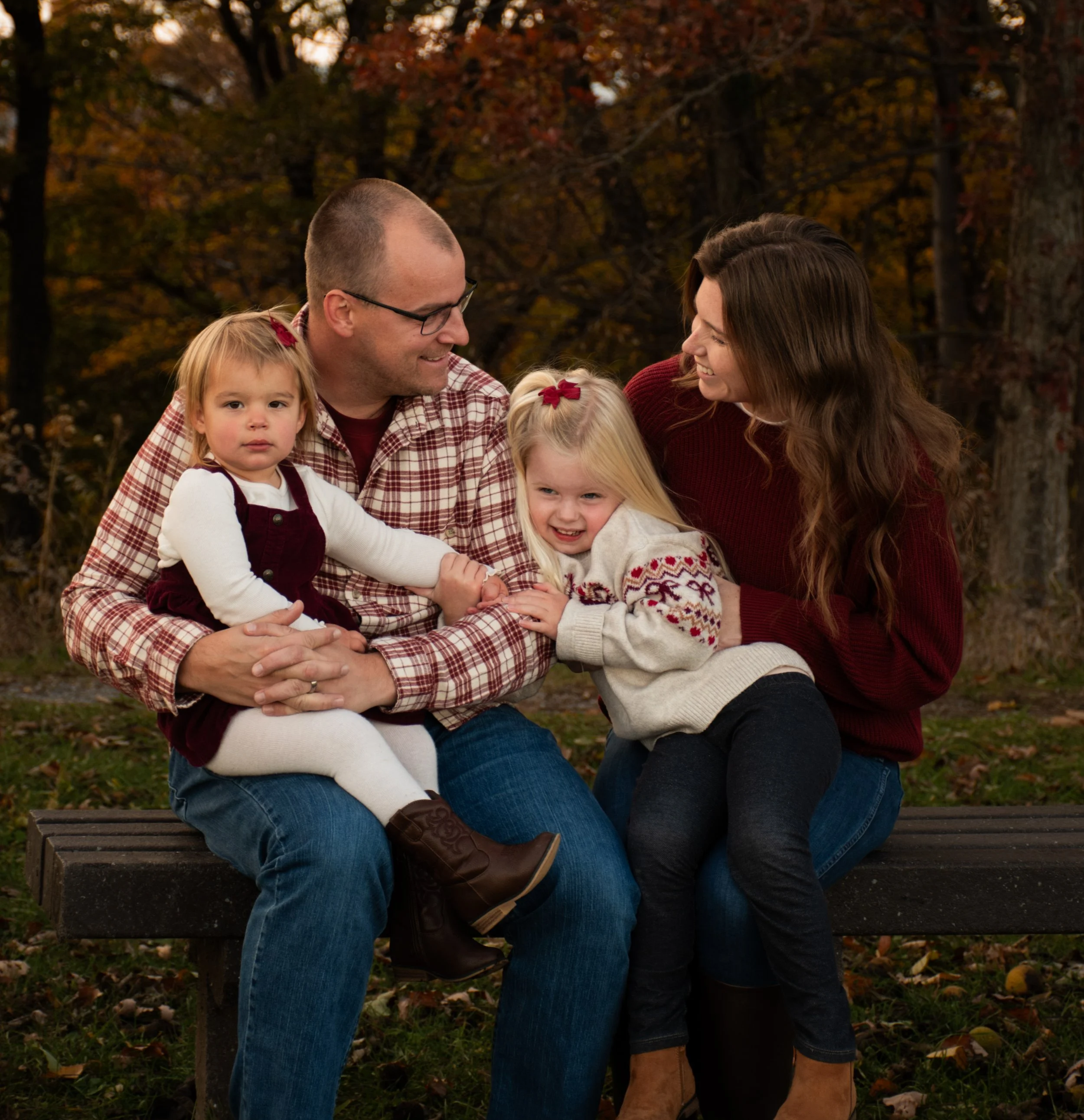 A family of four enjoying a playful moment outdoors during sunset in a field with rolling hills in the background.