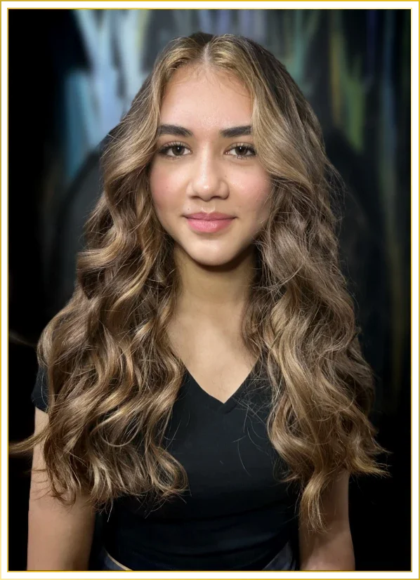 A young woman with long, wavy blonde hair, wearing a black top, smiling softly at the camera.