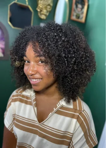 Young woman with natural curly hair smiling, wearing a striped shirt