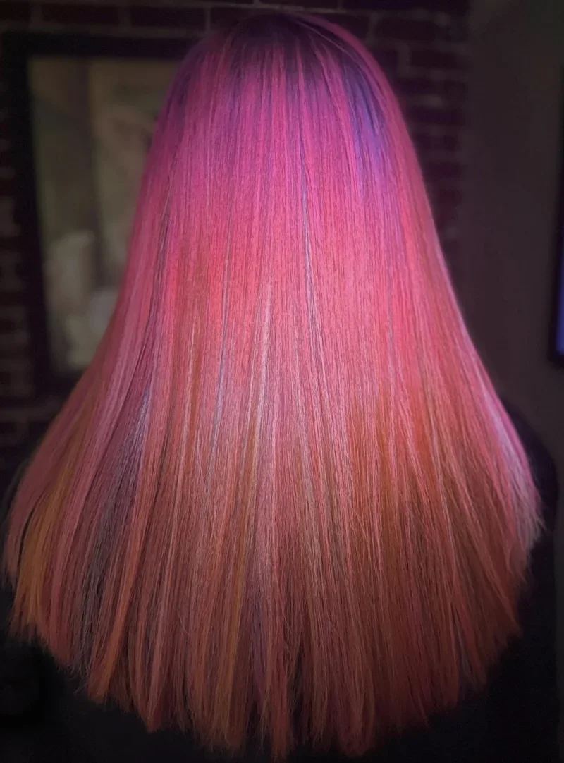 Back of a person's head with long straight hair dyed in pink, purple, and orange tones.