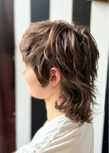 Side view of a woman with a layered, textured, medium-length hairstyle with highlights.