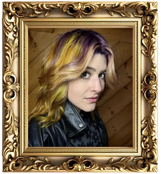 A woman with shoulder-length wavy blonde hair with purple and yellow highlights, looking over her shoulder at the camera, inside a decorative gold frame.