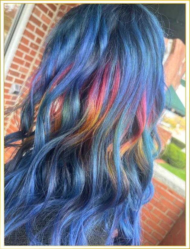 Hair dyed with a rainbow pattern including blue, pink, orange, yellow, green, and purple shades, styled in loose waves.