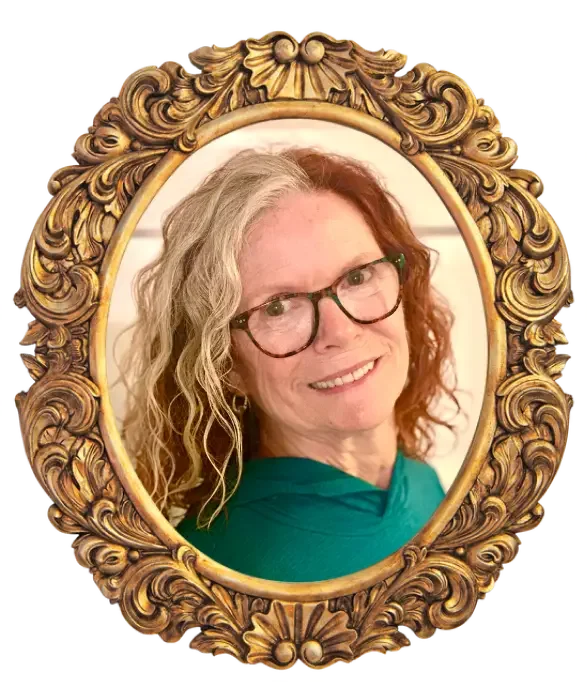 A woman with curly blonde hair and glasses smiling in an ornate gold oval picture frame.
