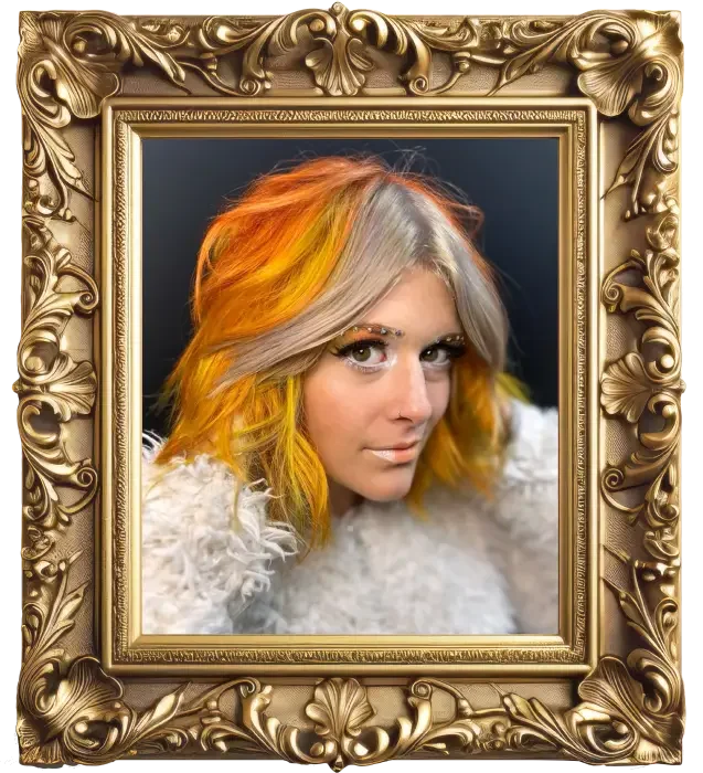 A woman with colorful hair, blending blonde, orange, and yellow shades, is seen wearing a fluffy white garment and has makeup with decorative eyebrows. The image is framed in an ornate gold picture frame.