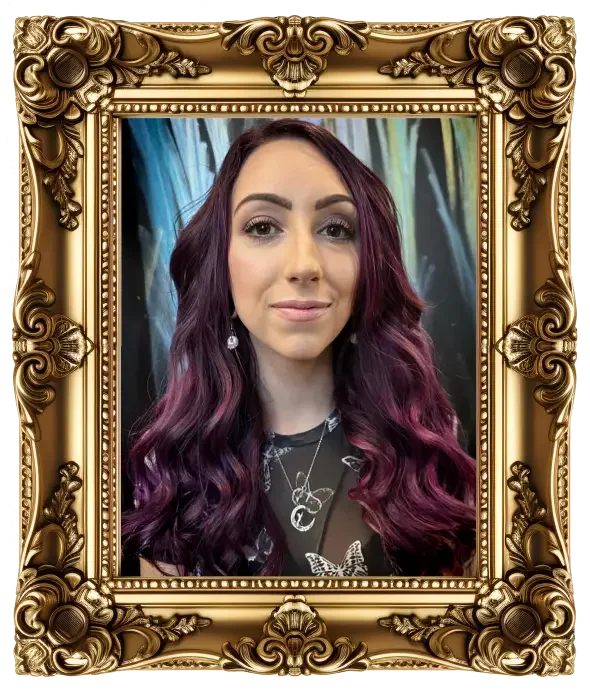 A woman with long, wavy hair that is dark at the roots and transitions to purple towards the ends. She is smiling slightly and wearing earrings and layered necklaces. The background features colorful abstract art. The image is framed by an ornate, gold decorative border.